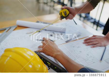 multi ethnic engineer brainstorming and measuring for cost estimating on blueprint and floor plan drawings about design architectural and engineering for houses and buildings. 108875911