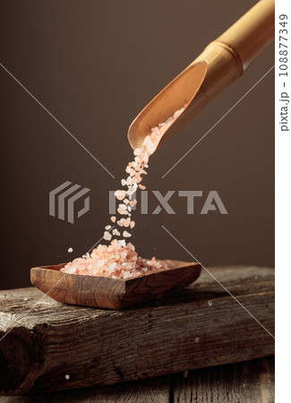 Pink salt is poured with a wooden spoon in the wooden dish. Pink salt is poured with a wooden spoon in the wooden dish. 108877349
