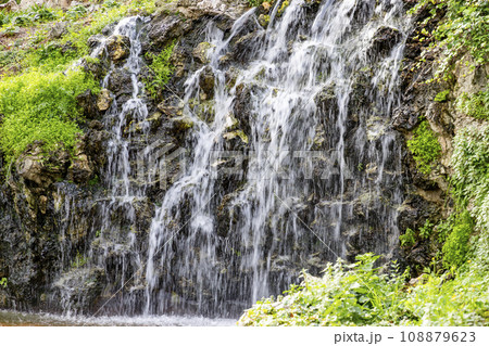 Waterfall. Waterfall in a park in Madrid. Artificial Mountain of Buen Retiro, called Mountain of the Cats. Dark stone background surrounded by green vegetation and plants and leaves. Autumn colors. 108879623