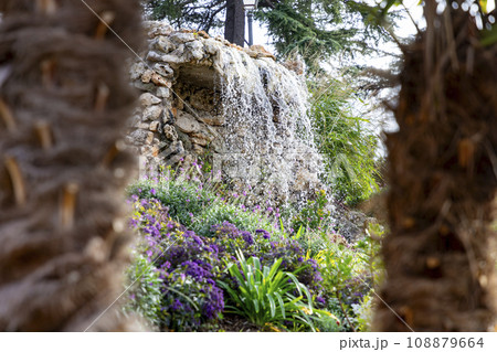 Waterfall. Waterfall in a park in Madrid. Artificial Mountain of Buen Retiro, called Mountain of the Cats. Dark stone background surrounded by green vegetation and plants and leaves. Autumn colors. 108879664