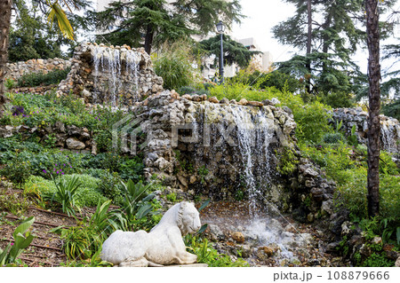 Waterfall. Waterfall in a park in Madrid. Artificial Mountain of Buen Retiro, called Mountain of the Cats. Dark stone background surrounded by green vegetation and plants and leaves. Autumn colors. 108879666