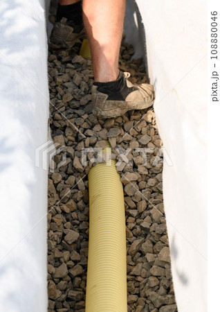 A worker stands in a drainage trench with white geotextile. Feet of the craftsman on the granite rubble closeup. A worker stands in a drainage trench with white geotextile. Feet of the craftsman on the granite rubble closeup. 108880046