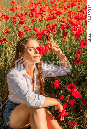 Woman poppies field. Happy woman is resting in the rays of the sun sitting in the poppy field. 108880316