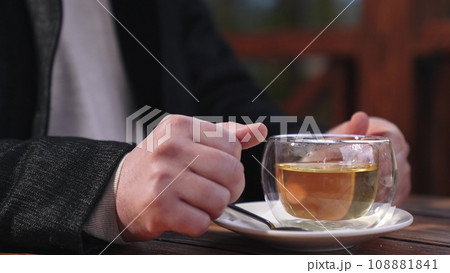 Man enjoys drinking hot tea in wooden cafe gazebo looking to side in cold autumn weather. Calmness and pleasure from man drinking hot tea in cafe gazebo. Gazebo of cafe and man drinking hot tea Man enjoys drinking hot tea in wooden cafe gazebo looking to side in cold autumn weather. Calmness and pleasure from man drinking hot tea in cafe gazebo. Gazebo of cafe and man drinking hot tea 108881841