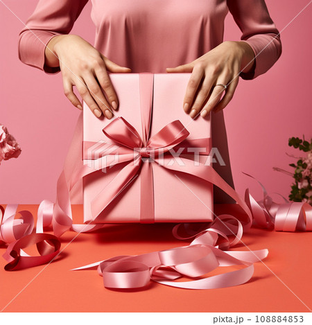 Female hands hold a pink gift box with a satin bow on a pink background Female hands hold a pink gift box with a satin bow on a pink background 108884853