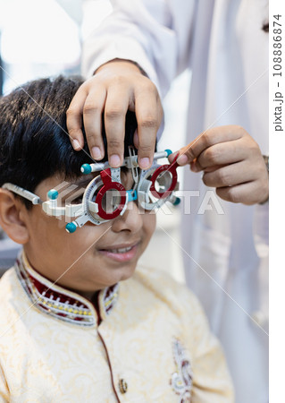 Happy Indian child boy examining eyesight modern ophthalmology equipment in clinic. 108886874