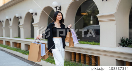Happy beautiful young stylish woman asian with shopping bag while walking near mall on holiday Black Friday 108887354