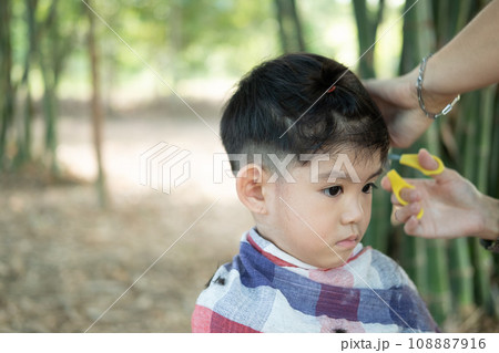 Barber cutting hair of an Asian boy In an open space filled with trees. Barber cutting hair of an Asian boy In an open space filled with trees. 108887916