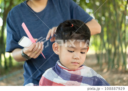 Barber cutting hair of an Asian boy In an open space filled with trees. Barber cutting hair of an Asian boy In an open space filled with trees. 108887929