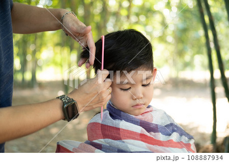 Barber cutting hair of an Asian boy In an open space filled with trees. Barber cutting hair of an Asian boy In an open space filled with trees. 108887934