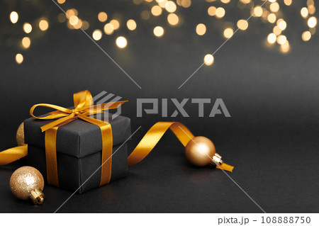 Black gift box with golden ribbon bow on black background 108888750
