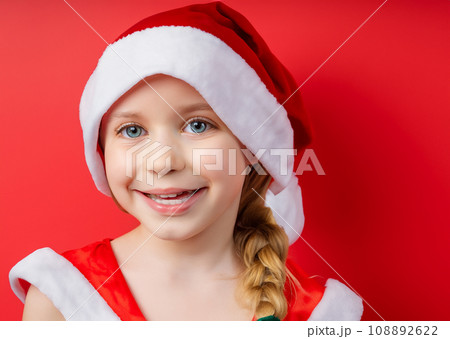 クリスマクリスのイメージの人物写真、サンタクロースの帽子をかぶった若い笑顔の白人の少女　AI生成画像 108892622