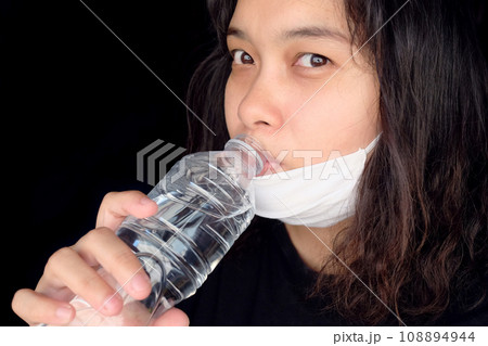 Asian Thai woman wearing a white cloth mask for prevent the Covid-19 or Corona virus and Air Pollution Value Pm 2.5 in Thailand and drinking a bottled mineral water. Health and illnes concept 108894944
