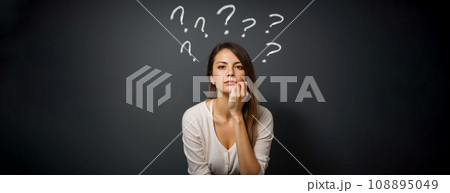 Young woman with question mark on gray background. minded woman touch hand chin. think thoughts about life problems. isolated over dark gray background Young woman with question mark on gray background. minded woman touch hand chin. think thoughts about life problems. isolated over dark gray background 108895049