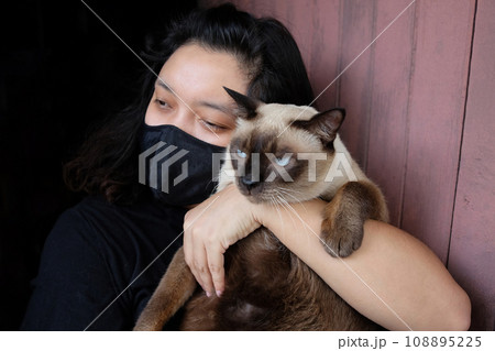 Asian Thai woman carrying a siamese cat and wearing a black cloth mask for prevent the Covid-19 or Corona virus and Epidemic disease at Thailand and around the world. Health and illness concept Asian Thai woman carrying a siamese cat and wearing a black cloth mask for prevent the Covid-19 or Corona virus and Epidemic disease at Thailand and around the world. Health and illness concept 108895225