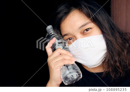Asian Thai woman wearing a white cloth mask for prevent the Covid-19 or Corona virus and Air Pollution Value Pm 2.5 in Thailand and hand holding a bottled mineral water. Health and illnes Concept 108895235