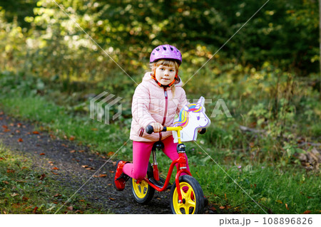 Child riding balance bike. Kids on bicycle in sunny forest. Little girl enjoying to ride glider bike on warm day. Preschooler learning to balance on run bicycle in safe helmet. Sport activity 108896826