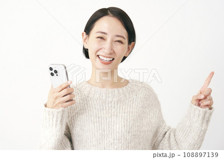 スマホを持って右側を指差すミドルエイジの女性 白背景 スマホを持って右側を指差すミドルエイジの女性 白背景 108897139