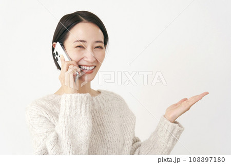 スマホで電話をしながら右側を手の平で指すミドルエイジの女性　白背景 108897180