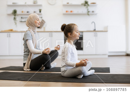Calm mother and little daughter working out on yoga mats together at home. Calm mother and little daughter working out on yoga mats together at home. 108897785