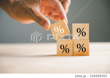Concept of interest rate and financial rates. Hand placing a wooden cube block on top, symbolizing an increase, with an upward direction icon and percentage symbol. 108898405