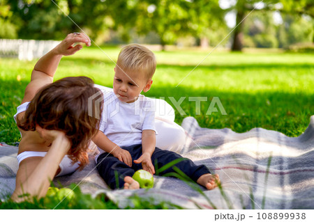 Mom in white clothes rests with her child in the park on green grass. Happy parenting outside. Lifestyle. 108899938