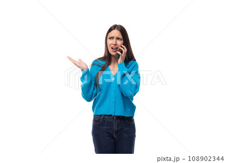 young beautiful European brunette woman dressed in a blue cardigan speaks on the phone while young beautiful European brunette woman dressed in a blue cardigan speaks on the phone while 108902344
