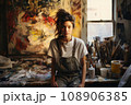 Portrait of young brunette female artist, wearing a worn-out denim apron 108906385