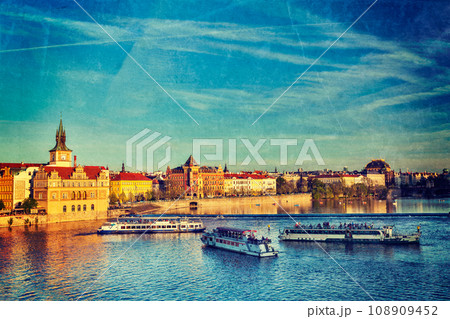 Vintage retro hipster style travel image of Vltava river with tourist boats and Prague Stare Mesto embankment view from Charles bridge on sunset with grunge texture overlaid. Prague, Czech Republic 108909452