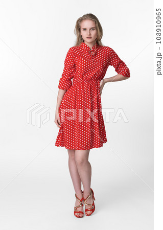 Young blonde woman dressed in summer red polka dot dress standing and poses on white background 108910965