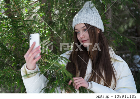 Portrait of teenager girl 17 year old using cellphone on pine forest, holding smartphone in hand 108911185