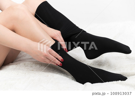 Close-up of female hands carefully putting on tight black tights. Crop view of woman sitting on bed 108913037