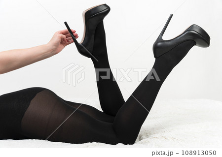 Woman in tights and high heels lies with legs bent in knees and raised up. Hand holds shoes by heel 108913050
