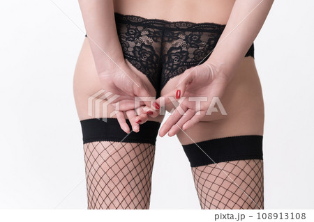 Rear view of female buttocks in knickers and legs in fishnet hose. Woman holds hands on back of butt 108913108
