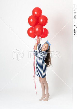 Girl holding large bunch red balloons in hands, smiling and looking at camera on white background 108913286