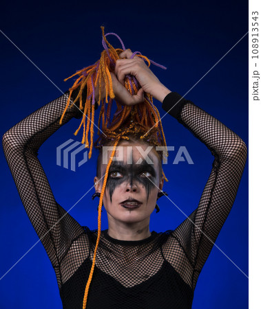 Informal young female with colored braids hairdo and spooky black stage makeup painted on face Informal young female with colored braids hairdo and spooky black stage makeup painted on face 108913543