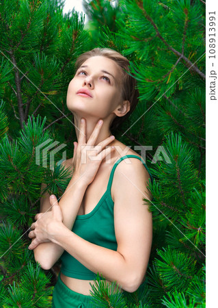 Portrait of blonde woman with short hair looking up, poses on background of shrub of Pinus Pumila Portrait of blonde woman with short hair looking up, poses on background of shrub of Pinus Pumila 108913991