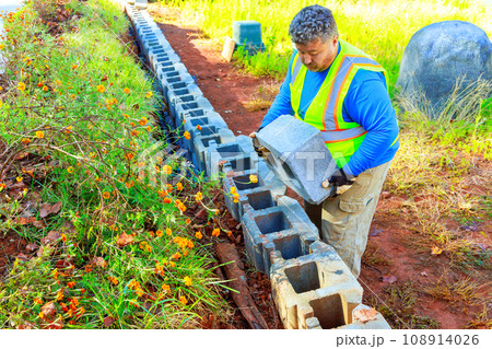 An employee of construction company mounts concrete blocks to retaining wall An employee of construction company mounts concrete blocks to retaining wall 108914026