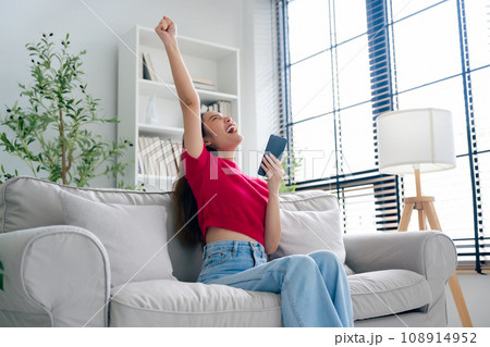 Happy young asian woman relax on comfortable couch at home texting messaging on smartphone Happy young asian woman relax on comfortable couch at home texting messaging on smartphone 108914952