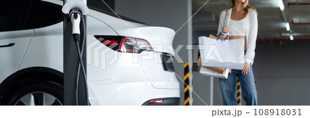 Young woman travel with EV electric car to shopping center parking lot innards Young woman travel with EV electric car to shopping center parking lot innards 108918031