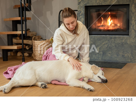 Woman sitting with dog near fireplace Woman sitting with dog near fireplace 108923268