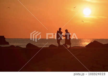 夕暮れの海岸を歩くカップルのシルエット 108924019