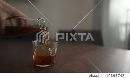 pour cold brew coffee over ice ball in tumbler glass on walnut table 108927424