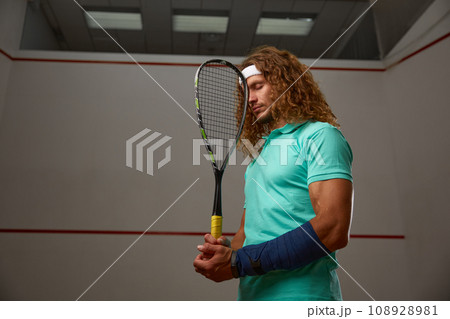 Young pensive racketball player with racket standing backside 108928981
