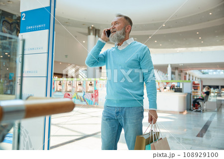 Stylish senior man with phone walking with purchases Stylish senior man with phone walking with purchases 108929100