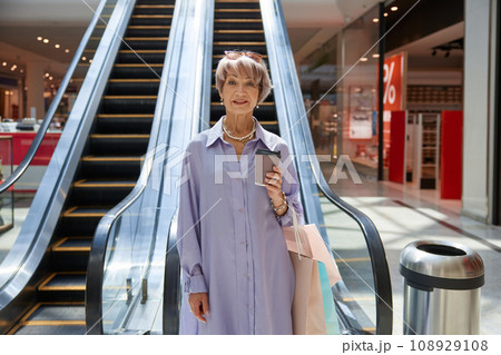 Happy retired woman riding on escalator at shopping mall 108929108