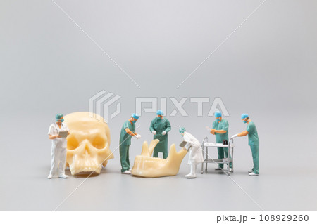 Miniature people Doctor with a giant human skull on a grey background 108929260