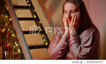 Young woman got scared and nervous on Christmas night. Police or ambulance car lights illuminating the room. Crime, ambulance, injury, problems with law and theft on winter holidays and celebrations. Young woman got scared and nervous on Christmas night. Police or ambulance car lights illuminating the room. Crime, ambulance, injury, problems with law and theft on winter holidays and celebrations. 108930507