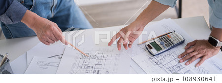 Two engineer architect pointing on blueprint of sketching interior architectural building to discussion technical for construction plan and building model while working together in workplace site Two engineer architect pointing on blueprint of sketching interior architectural building to discussion technical for construction plan and building model while working together in workplace site 108930641