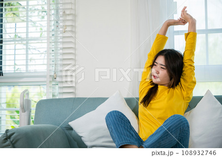 Happy woman stretch oneself for relaxing activity feeling lazy on weekend on couch, resting napping break, Lifestyle Asian young female stretching her arms on sofa in the living room at home 108932746